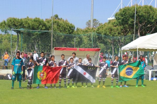 Equipe sub-12 do Vasco entrando em campo com a bandeira do clube, e de Brasil e Portugal.