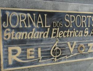 Placa na esttua exibe os nomes do JS , da Rei da Voz e da Standard Electrica