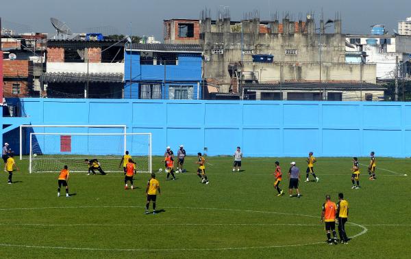Vasco trabalha enquanto vizinhos observam da janela e da laje atrs do gol sem arquibancada