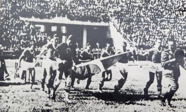 Equipe do Palmeiras entra em campo em partida do Paulista de 1942, exibindo uma bandeira do Brasil.  direita, fardado, o capito Adalberto Mendes